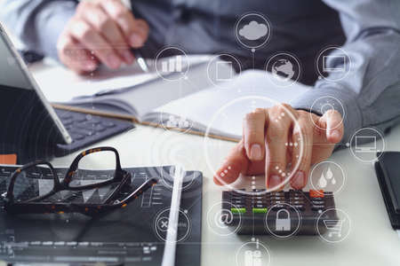 businessman hand working with finances about cost and calculator and latop with mobile phone on withe desk in modern office with VR icon diagramの写真素材
