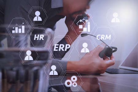 Architecture of ERP (Enterprise Resource Planning) system with connections between business intelligence (BI), production, CRM modules and HR diagram.Man using VOIP headset with digital tablet computer.の写真素材