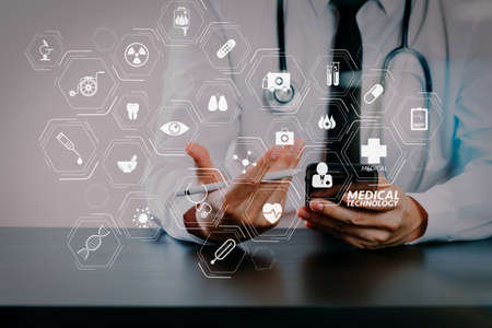 Modern VR with medical technology diagram concept.close up of smart medical doctor working with smart phone and stethoscope on dark wooden desk with glass reflected viewの写真素材