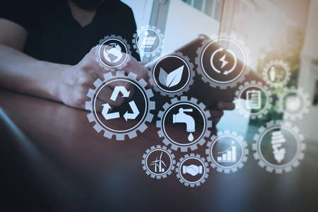 Sustainable development with icons of renewable energy and natural resources preservation with environment protection inside connected gears.businessman working with digital tablet computer on wooden desk as conceptの写真素材