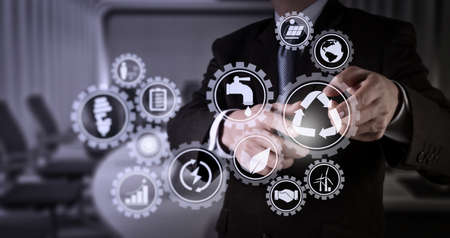 Sustainable development with icons of renewable energy and natural resources preservation with environment protection inside connected gears.Businessman hand pressing an imaginary button on virtual screenの写真素材