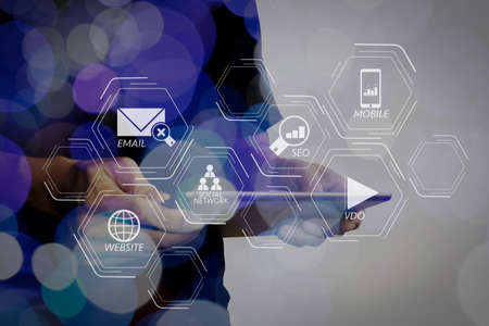 Digital marketing media (website ad, email, social network, SEO, video, mobile app) in virtual screen.Double exposure of businessman hand using Tablet computer with colour cloud concept.の写真素材