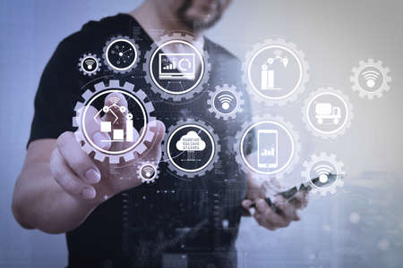 Smart factory and industry 4.0 and connected production robots exchanging data with internet of things (IoT) with cloud computing technology.Businessman hand pressing an imaginary button,holding smart phone.の写真素材