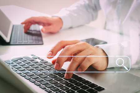 Searching Browsing Internet Data Information Networking Concept with blank search bar.close up of businessman typing digital tablet with keyboard and laptop computer on white desk in modern officeの写真素材