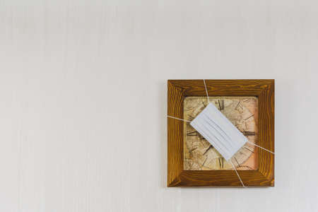 Wall clock on a white wall, copy space, the clock is wearing a medical mask.の写真素材