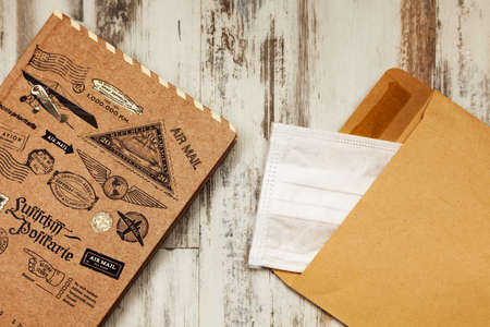 Notebook and envelope are on a wooden table, in the envelope is a medical maskの写真素材