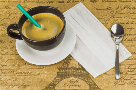 A Cup of coffee with a pencil, a medical mask and a spoon under a saucer.の写真素材
