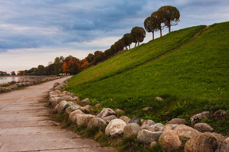Green hill with a path lined with stones, autumn trees on the hill, sky background.の写真素材