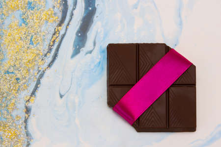 A piece of chocolate tied with a gift ribbon on a multicolored light background, top view.の写真素材
