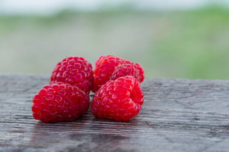 Raspberries are lying on a wooden table, the background is blurred.