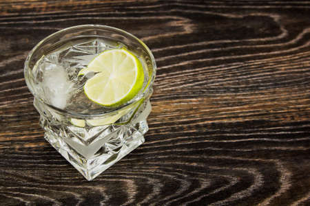 A glass of cold drink with lime and ice on a wooden textured table, close-up.の写真素材