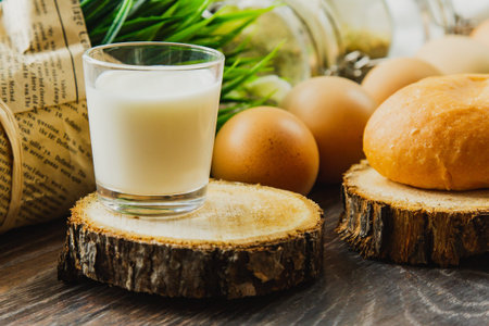 A hamburger bun and a glass of milk lie on a section of a tree trunk with brown eggs and spices salt...