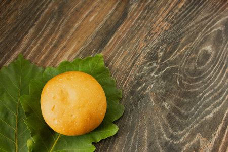 A hamburger bun sits on a green oak leaf on a wooden textured table, close up.