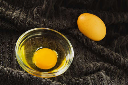 Brown chicken egg and a bowl with a broken egg laid out in a row on a background of gray fabric, egg yolk, farm products, natural eggs.の写真素材