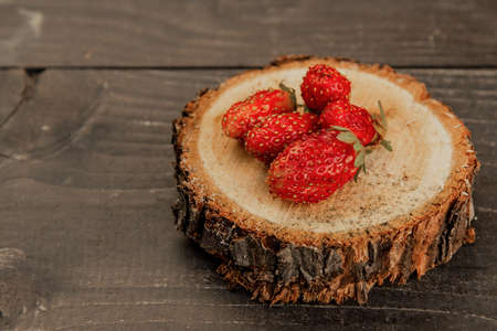 Strawberries are lying on the sawn tree trunk on a wooden table, close up.の写真素材