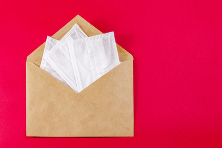 Medical face mask in a gray envelope on a red background, close-up.