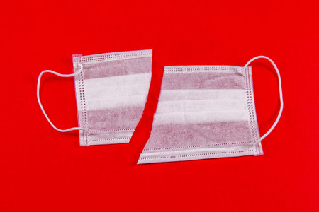 Concept of the end of the coronavirus, Covid-19, medical mask, white mask cut in half on a red...