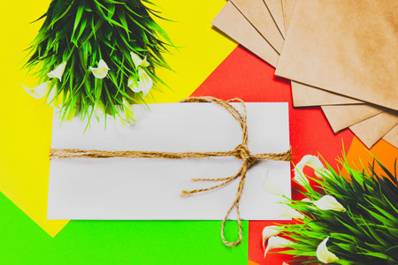 White envelope, envelope wrapped with rope, multicolored background with a white flower and green...