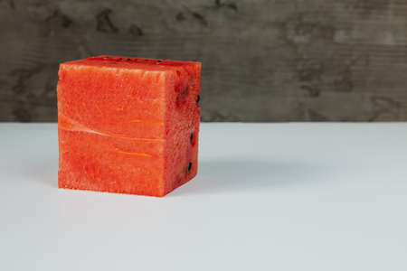 A cube-shaped watermelon on a white and gray concrete background.の写真素材