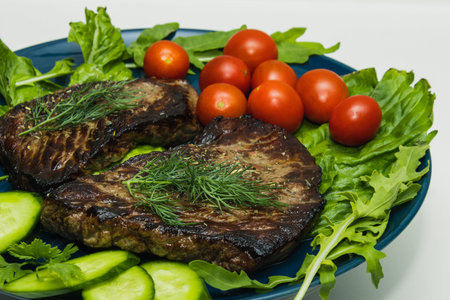Beef steaks on a plate with cucumber, tomato and herbs.