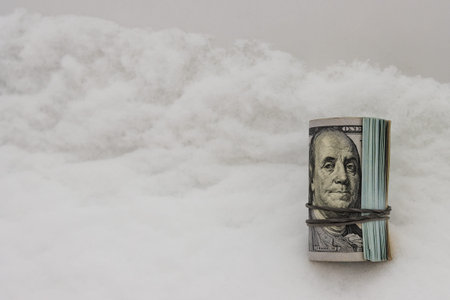 A dollar in winter, a roll of twisted dollar bills lying on the snow, close-up.