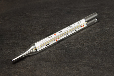 Mercury classic body thermometer, lying on a black textured background, degrees Celsius.