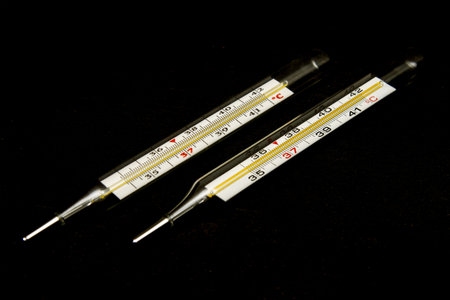 Mercury classic medical body thermometer, two thermometers lie on a black wood textured background,...