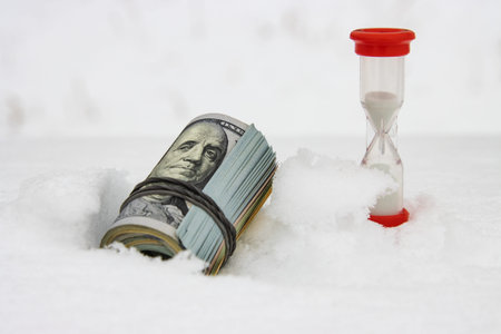 A dollar in winter, a roll of rolled dollar bills lying on the snow with a red hourglass, close-up,...