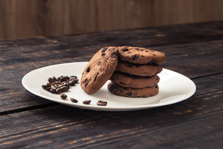 chocolate chip cookies on a white plate with coffee beans on dark wooden tableの写真素材
