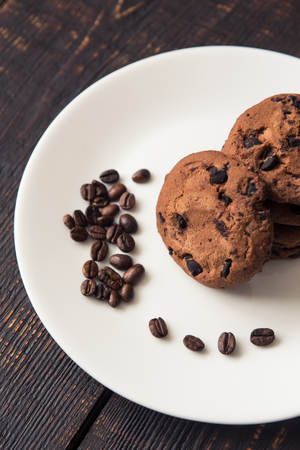 chocolate chip cookies on a white plate with coffee beans on dark wooden tableの写真素材