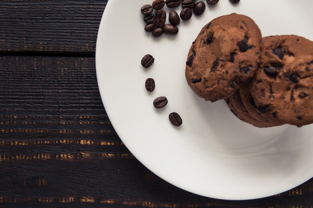 chocolate chip cookies on a white plate with coffee beans on dark wooden tableの写真素材