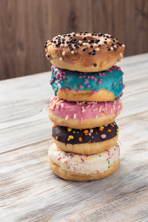 glazed donuts with sprinkles folded in pile on white wooden tableの写真素材