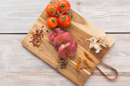 beef steak with vegetables and spices on a cutting Board, a white wooden tableの写真素材