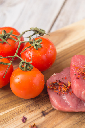 beef steak with vegetables and spices on a cutting Board, a white wooden tableの写真素材