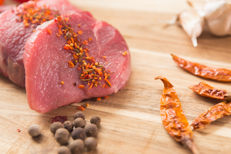 beef steak with vegetables and spices on a cutting Board, a white wooden tableの写真素材