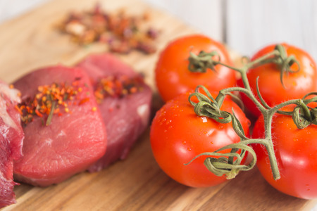 beef steak with vegetables and spices on a cutting Board, a white wooden tableの写真素材