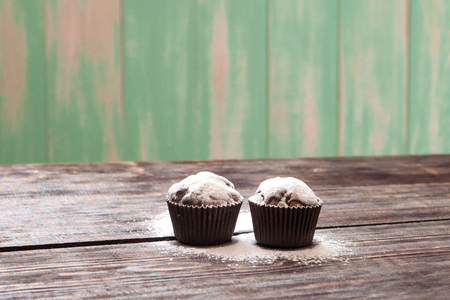 chocolate muffins sprinkled with powdered sugar on a dark wooden tableの写真素材
