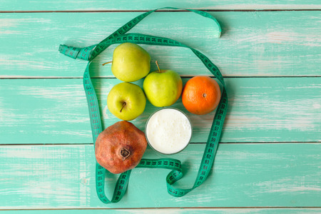 Apple, pomegranate, orange and glass with kefir and measuring tape on green wooden background, top viewの写真素材
