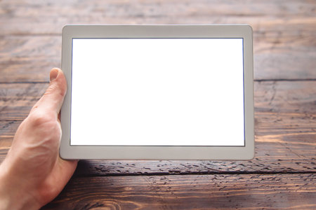 men's hand holding tablet with blank screen for your logo or design on dark wooden table