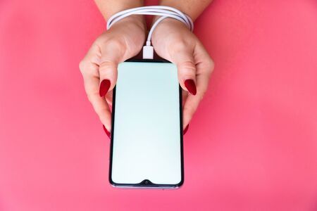 Top view woman's hands having modern smartphone, blank screen for your text or design. Hands bound with telephone charger or cable. Addictions on social networking sites, internet and gadgets .の写真素材