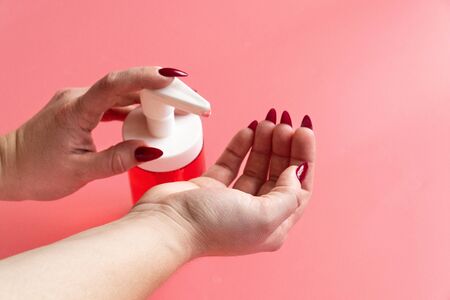 Side view women's hands squeeze out liquid soap on pink background. Hygiene concept hand detail.の写真素材