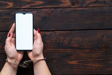 Top view woman hands in handcuffs hold a smartphone with an blank screen for text. The concept of internet addiction, social networking and gadgets.の写真素材