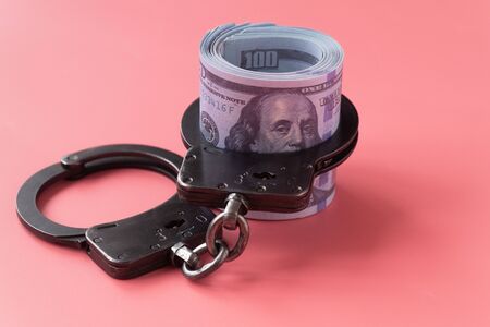 twisted wad of dollars buttoned with handcuffs on a pink backgroundの写真素材