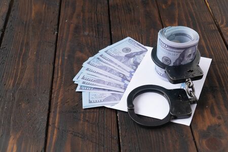 twisted wad of dollars buttoned with handcuffs on wooden background, envelope with moneyの写真素材