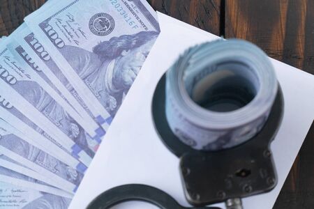 twisted wad of dollars buttoned with handcuffs on wooden background, envelope with moneyの写真素材