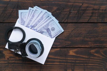Close up twisted wad of dollars buttoned with handcuffs on wooden background, envelope with moneyの写真素材