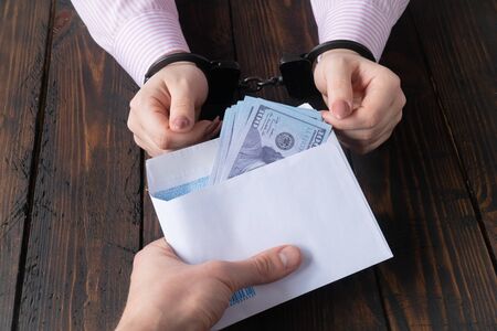 mens hands give money in envelope to womens hands in handcuffs against the background of a wooden tableの写真素材