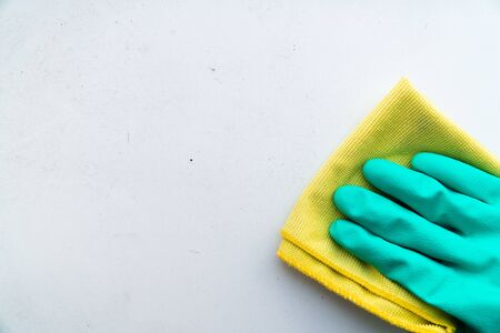 hand in green rubber glove wipes dust with yellow rag from white window sill or tableの写真素材