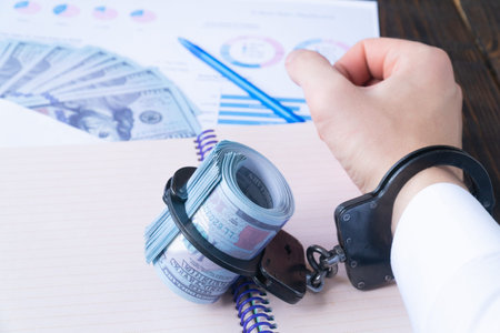 Mans hand and twisted hundred-dollar banknotes are buttoned up in handcuffs against the background...