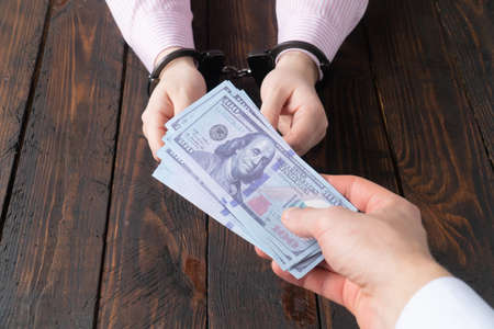 mens hands give money to womens hands in handcuffs against the background of a wooden tableの写真素材